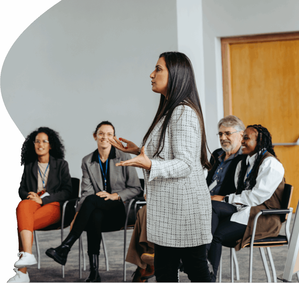 Frau hält einen Vortrag vor Teilnehmenden in einem Seminarraum.