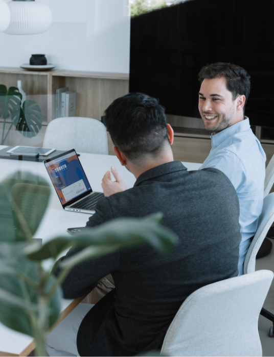 Zwei junge Männer sitzen an einem Tisch mit einem Laptop und bespprechen die organisatorischen Punkte für anstehende Veranstaltungen ihrer Akademie