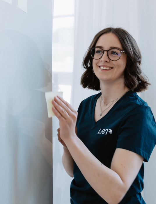 Eine junge Frau klebt Postits an ein Whiteboard, um anstehende Veranstaltungen und Seminare übersichtlich planen zu können.