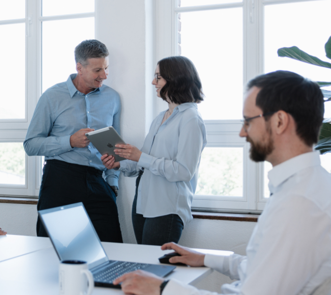 Ein junges, dynamisches Team stehen und sitzen zusammen vor einem Taplet und einem Desktop PC und gehen gemeinsam die anstehenden veranstaltungen digital durch.